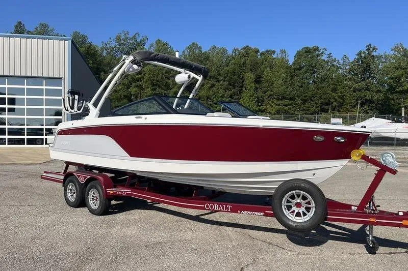 Slide: The Image of 2025 Cobalt CS23 Surf boat on trailer, red and white design, parked outdoors. - 20
