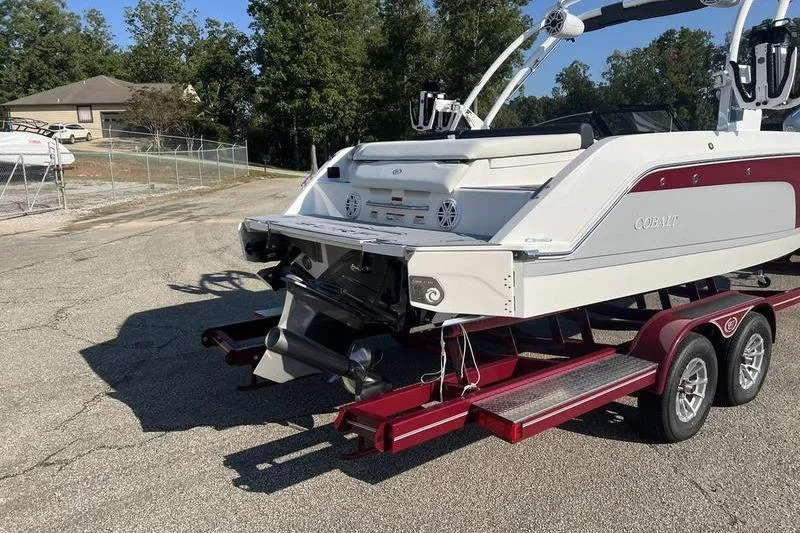 Slide: The Image of 2025 Cobalt CS23 Surf boat on a red trailer, parked outdoors. - 21