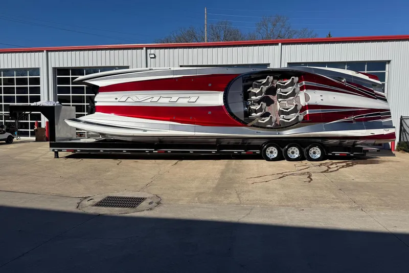 Slide: The Image of 2016 MTI 48 boat with red and white design on a trailer outside a garage. - 20