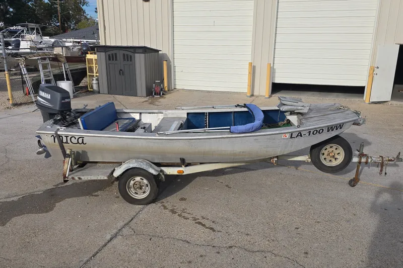 Slide: The Image of 1976 Custom Aluminum 16 boat on trailer with Yamaha motor, parked outside a garage. - 2