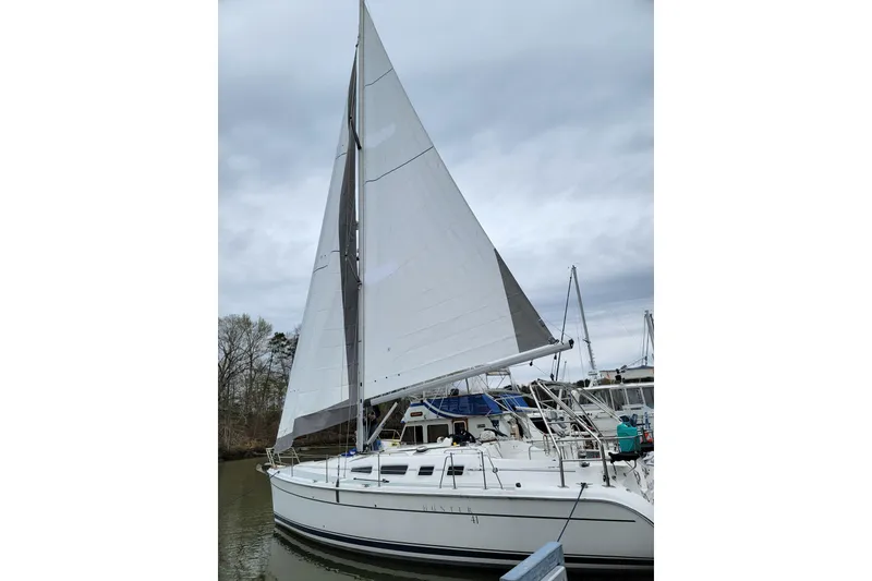 Slide: The Image of 2004 Hunter 41 AC sailboat docked with sails raised under cloudy skies. - 2