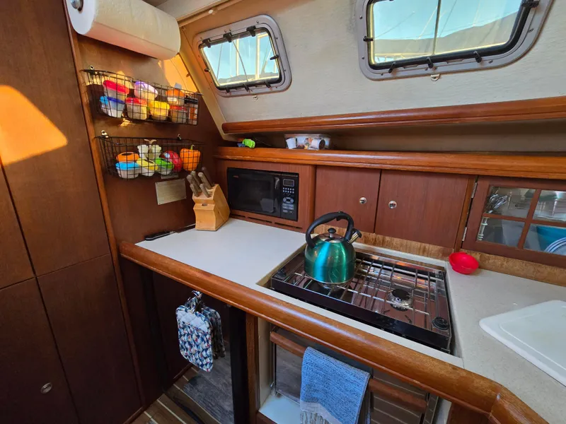 Slide: The Image of Cozy 2004 Hunter 41 AC sailboat kitchen with stove, microwave, and colorful storage baskets. - 24