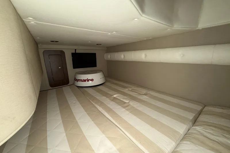 Slide: The Image of 2018 Rinker EX 320 cabin interior with striped bedding and Raymarine equipment. - 26