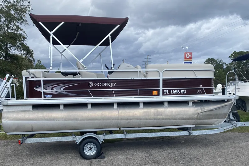 The Image of 2020 Godfrey 180 SR pontoon boat on trailer, under cloudy sky. - 1