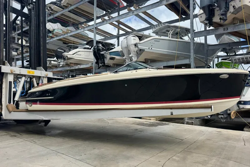 Slide: The Image of 2018 Chris-Craft Capri 27 boat in storage, black hull with red stripe, side view. - 12