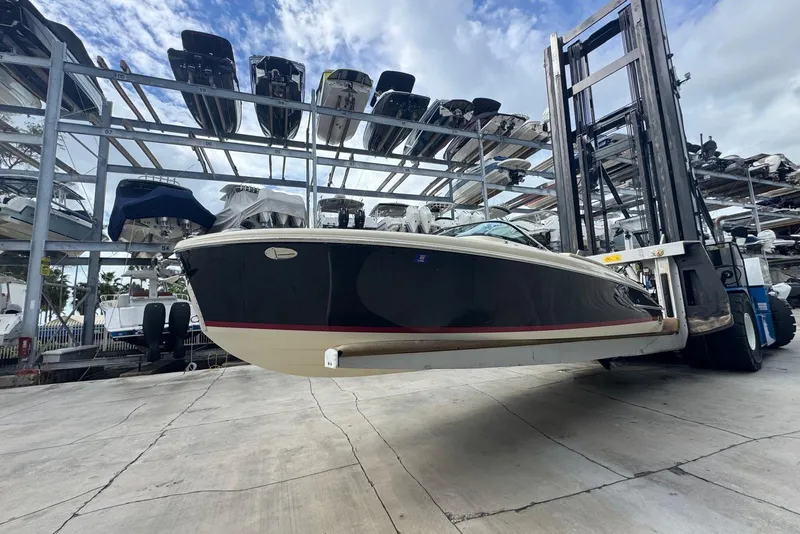 Slide: The Image of 2018 Chris-Craft Capri 27 boat lifted in storage facility under cloudy sky. - 13