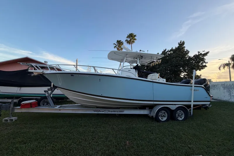 The Image of 2009 Mako 284 Center Console boat on trailer, parked on grass, with clear sky background. - 1