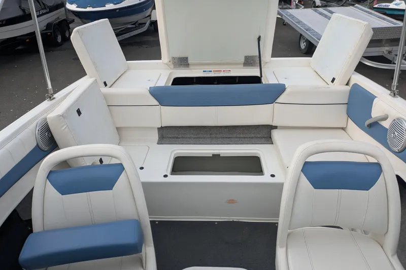 Slide: The Image of 2013 Bayliner 185 Bowrider interior with white and blue seating, open storage compartments. - 16