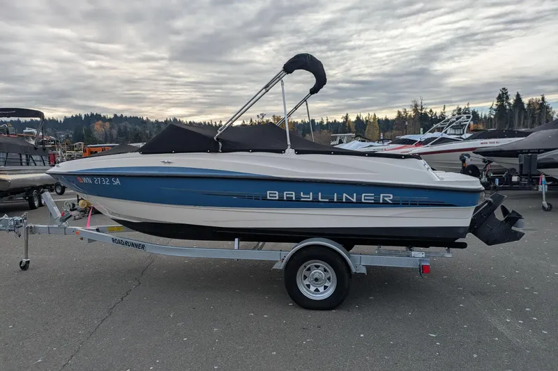 Slide: The Image of 2013 Bayliner 185 Bowrider on trailer, parked outdoors under cloudy sky. - 3