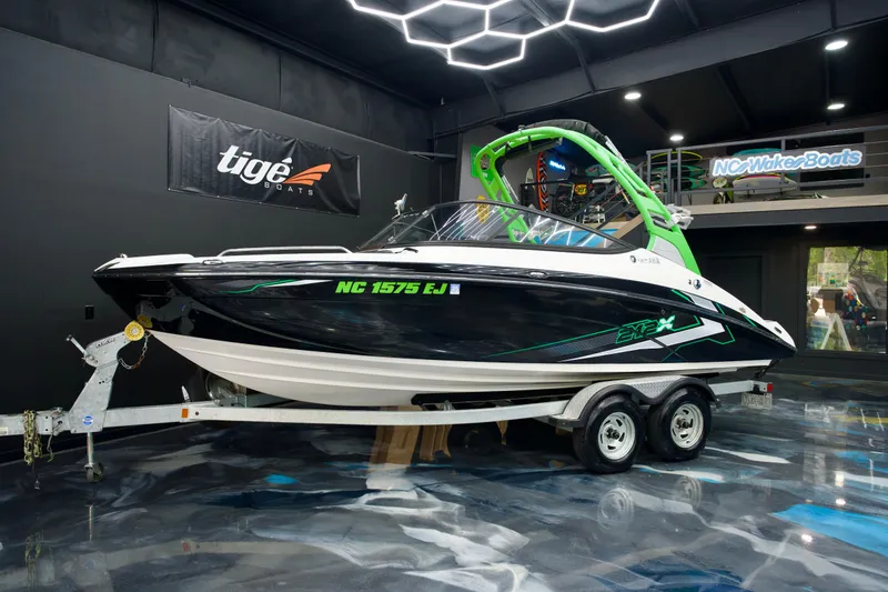 The Image of 2018 Yamaha Boats 212X on trailer in showroom, featuring sleek black and green design. - 1