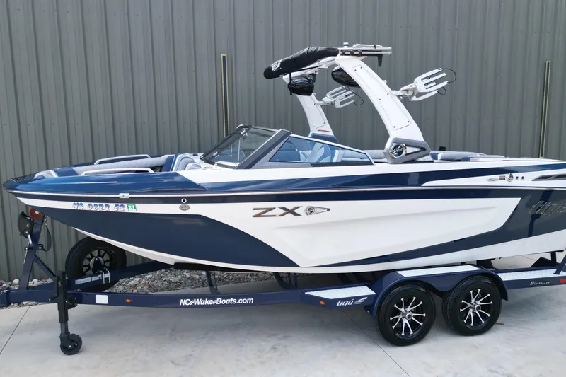 The Image of 2019 Tigé ZX1 boat on trailer, blue and white design, parked by a metal wall. - 1