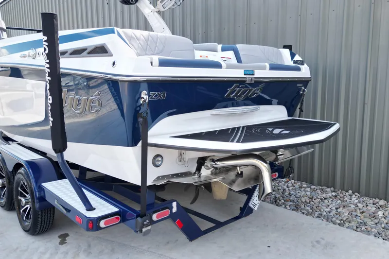 Slide: The Image of 2019 Tigé ZX1 boat on trailer, blue and white design, parked near a metal building. - 12
