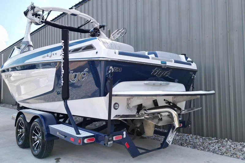 Slide: The Image of 2019 Tigé ZX1 boat on trailer, blue and white design, parked near a metal building. - 13