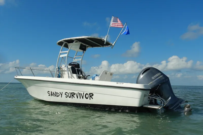 Slide: The Image of 2004 Hydra-Sports 212 CC boat named "Sandy Survivor" on calm water with flags. - 1
