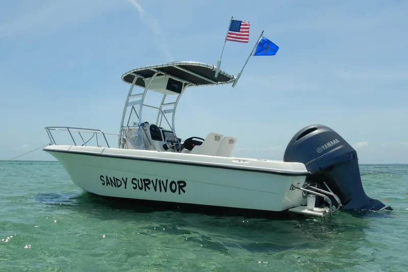 Slide: The Image of 2004 Hydra-Sports 212 CC boat named "Sandy Survivor" on clear water with flags. - 3