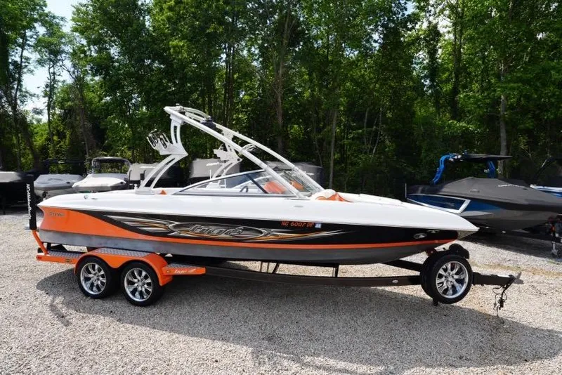 The Image of 2008 Tigé 24Ve boat on trailer, orange and white, parked outdoors. - 1