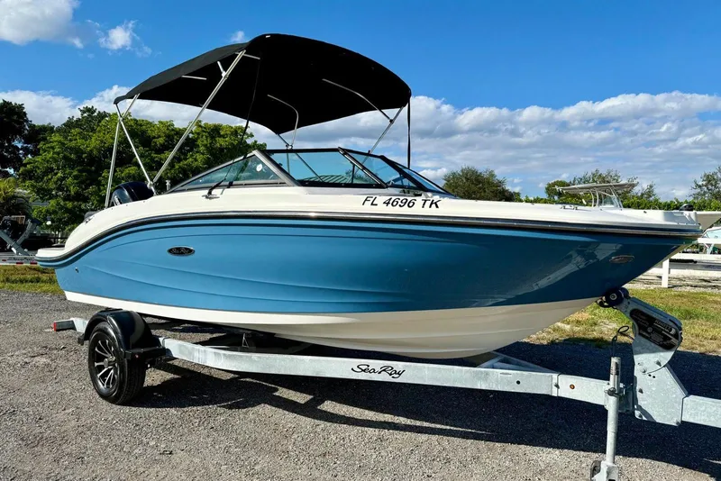 Slide: The Image of 2023 Searay SPX 190 boat on trailer, blue hull, black canopy, parked outdoors. - 2