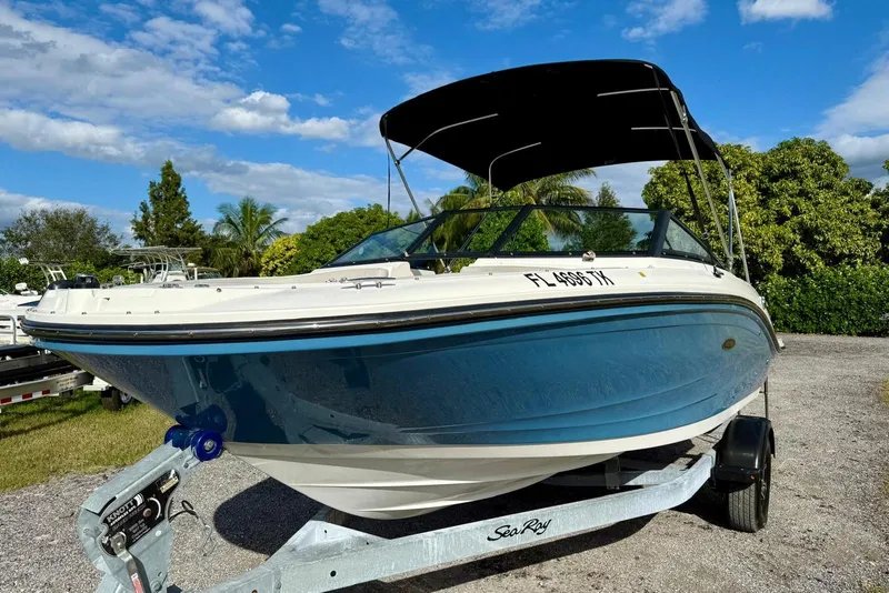 Slide: The Image of 2023 Searay SPX 190 boat on trailer, blue hull, sunny day, lush greenery background. - 3