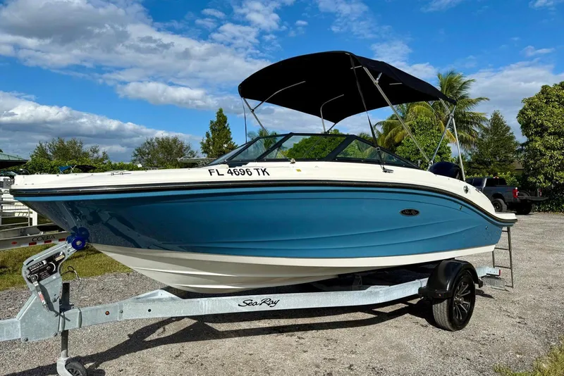 Slide: The Image of 2023 Searay SPX 190 boat on trailer, blue hull, sunny day, palm trees in background. - 4