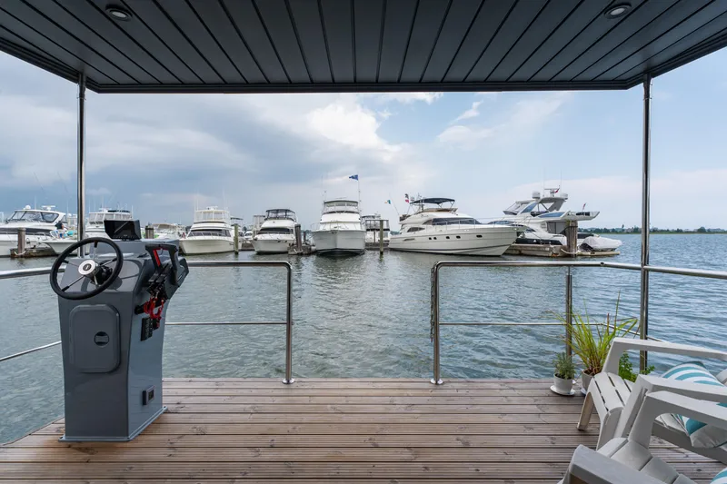 Slide: The Image of Houseboat deck view with steering console, overlooking marina with yachts. Waterlodge Apart L Long 2026. - 21