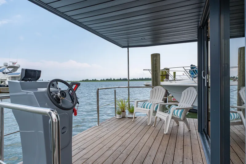 Slide: The Image of Modern Waterlodge Apart L Long houseboat deck with chairs, steering console, and scenic water view. - 23