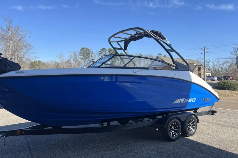Slide: The Image of 2025 Yamaha Boats AR250 in blue on a trailer, parked outdoors. - 26