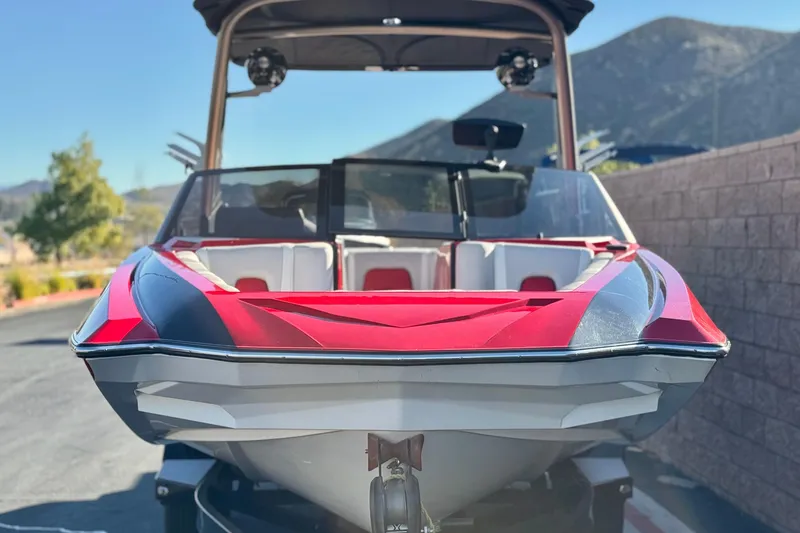 Slide: The Image of 2018 Malibu Wakesetter 21 MLX boat, red and black, parked outdoors with mountains in background. - 2