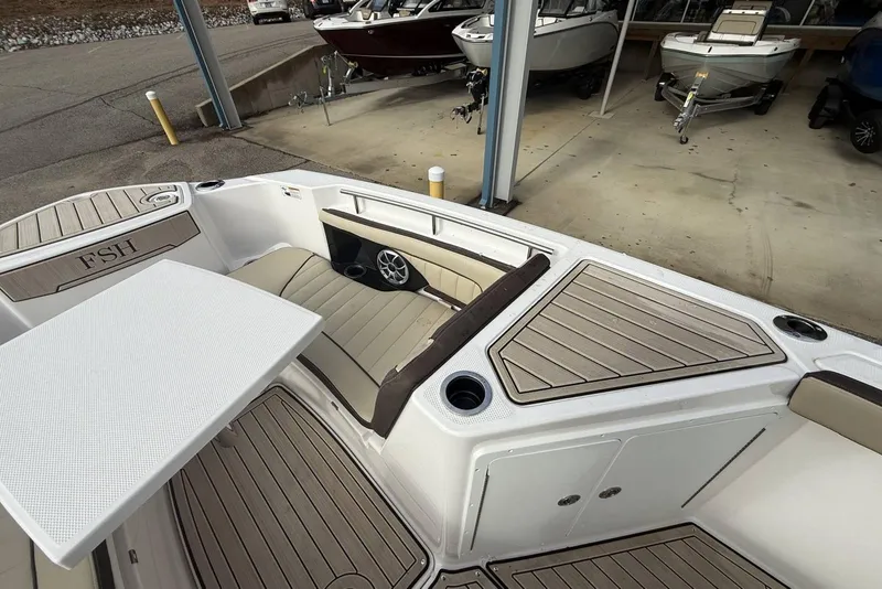 Slide: The Image of 2024 Yamaha Boats 255 FSH Sport E interior with seating and table, docked in a marina. - 19