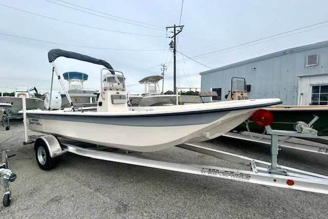 Slide: The Image of 2026 Carolina Skiff E20 JVX CC boat on trailer, parked outdoors near a warehouse. - 6