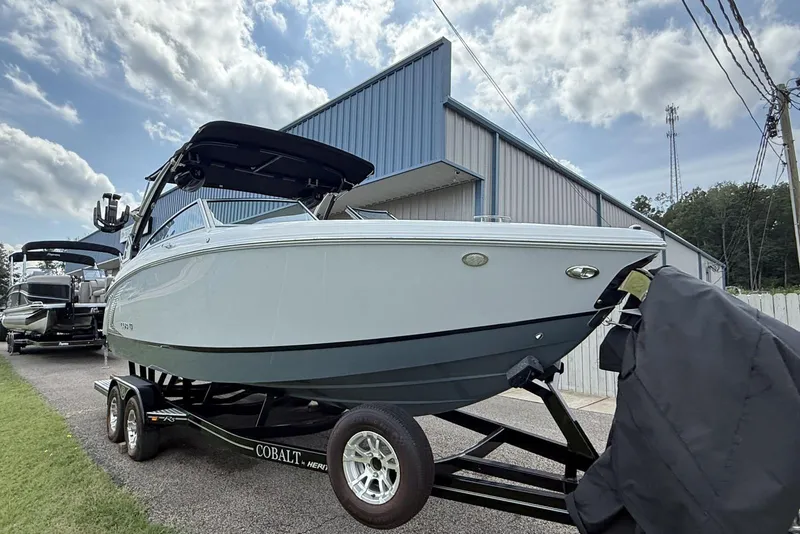 Slide: The Image of 2020 Cobalt R5 Surf boat on trailer, parked near a blue building under a cloudy sky. - 7