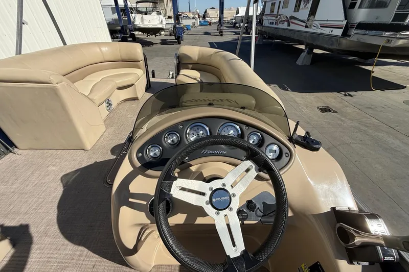 Slide: The Image of 2017 Manitou 230 boat interior with steering wheel and seating, docked near other boats. - 16