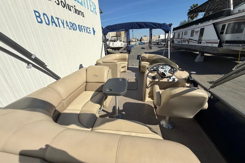 Slide: The Image of 2017 Manitou 230 pontoon boat with beige seating, docked near a boatyard office. - 22