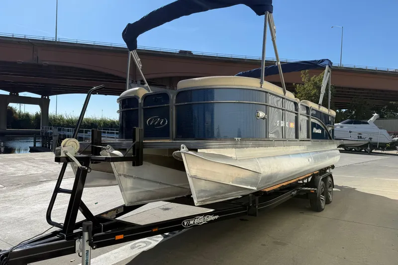Slide: The Image of 2017 Manitou 230 pontoon boat on trailer under bridge, sunny day. - 3