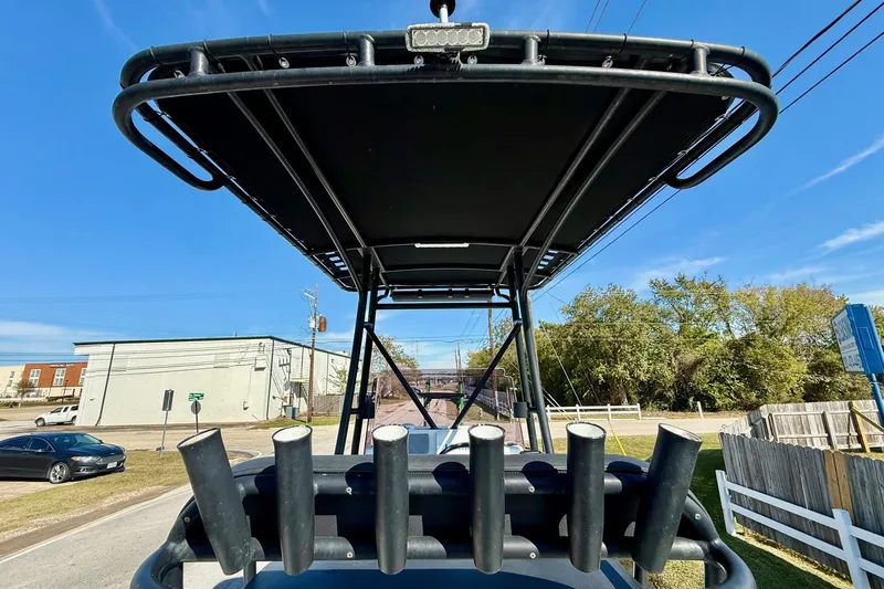 Slide: The Image of 2018 Shallow Sport 25 X3 boat with rod holders and canopy, parked outdoors. - 11