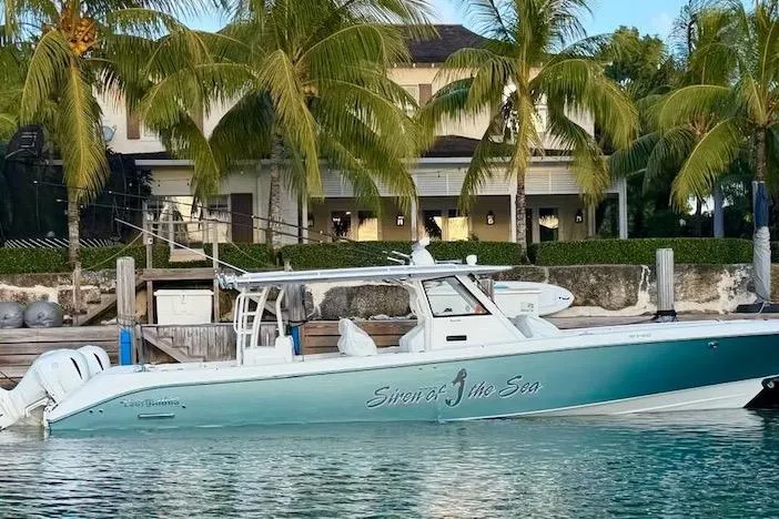 Slide: The Image of 2016 Everglades 435 Center Console boat docked by palm trees and a waterfront house. - 2