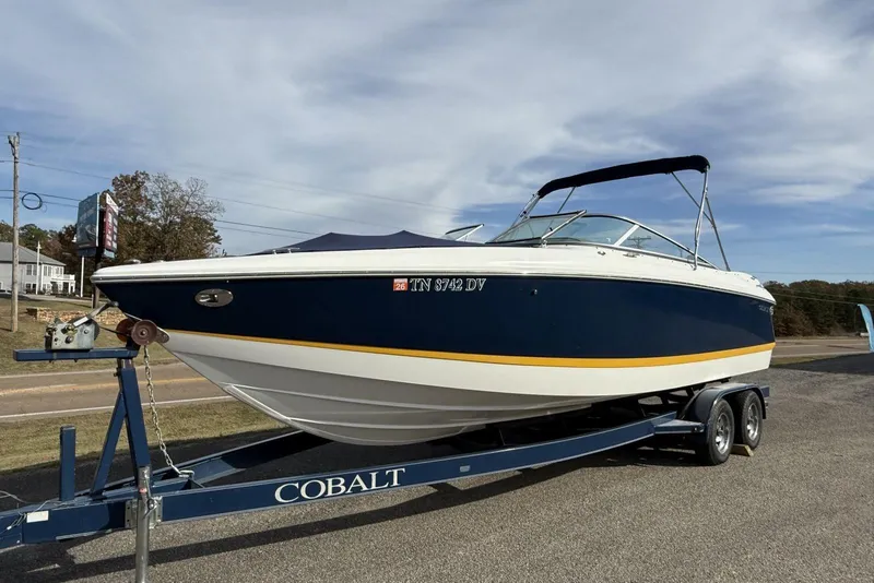 The Image of 2004 Cobalt 250 boat on trailer, blue and white design, parked outdoors. - 0