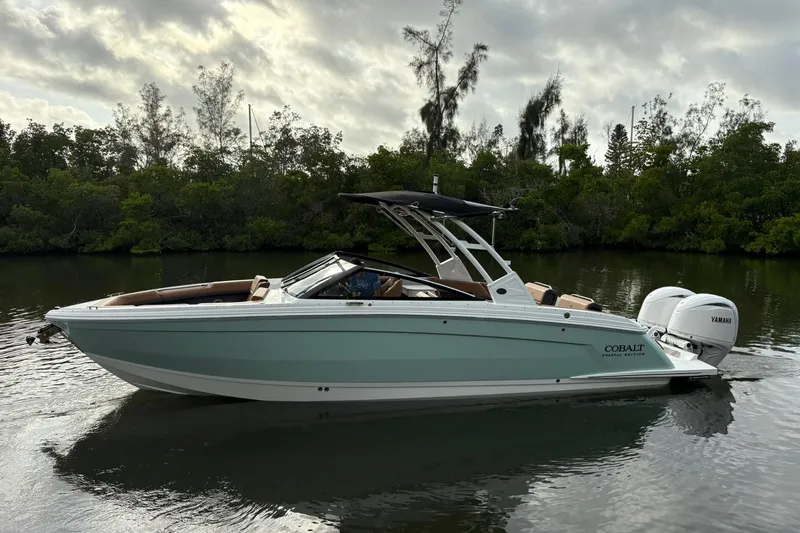 Slide: The Image of 2026 Cobalt R8 Outboard boat on calm water, surrounded by lush greenery. - 2