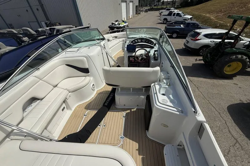 Slide: The Image of 2005 Crownline 288 BR boat interior with white seating and wood flooring, parked outdoors. - 12
