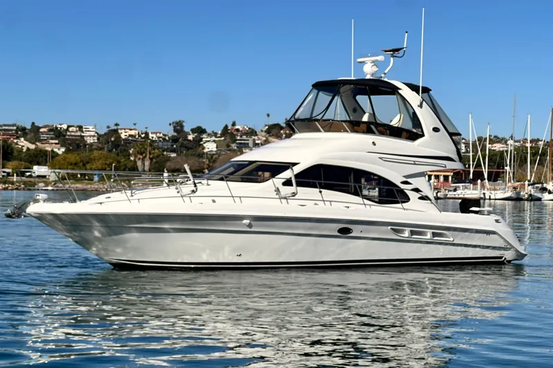 The Image of 2005 Sea Ray 420 Sedan Bridge yacht on calm water, with a scenic coastal backdrop. - 1