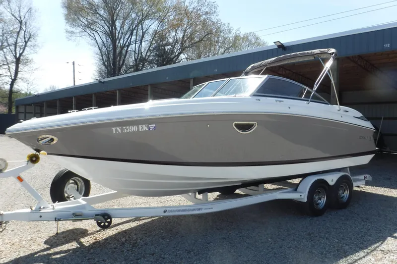 Slide: The Image of 2010 Cobalt 242 boat on trailer, parked outdoors, with trees and storage building in background. - 16
