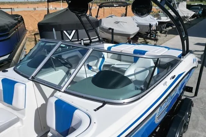 Slide: The Image of 2019 Chaparral 21 H2O Surf boat with blue and white interior, docked outdoors. - 11