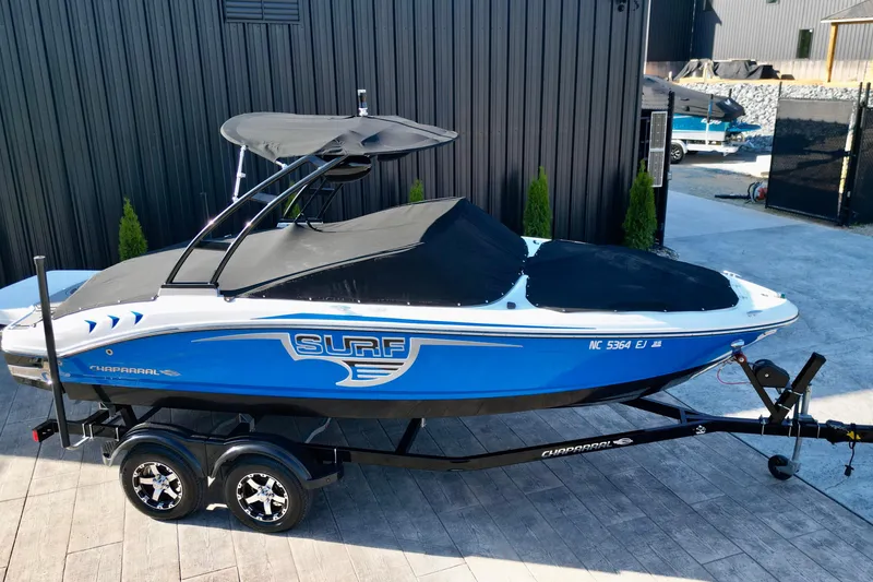 Slide: The Image of 2019 Chaparral 21 H2O Surf boat on trailer, blue and white, parked outdoors. - 19