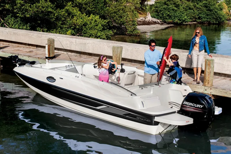 The Image of 2015 Bayliner 210 Deck Boat docked in marina with city skyline background. - 0