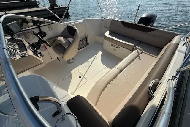 Slide: The Image of 2015 Bayliner 210 Deck Boat interior with seating and steering console, docked by the water. - 10