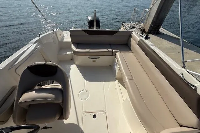 Slide: The Image of 2015 Bayliner 210 Deck Boat interior with beige seating, docked by the water. - 11