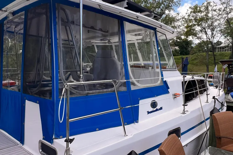 Slide: The Image of 2002 Endeavour Trawlercat 36 with blue canopy, docked in a scenic marina setting. - 11