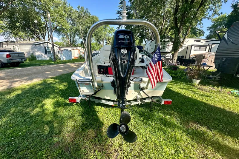 Slide: The Image of 2014 Boston Whaler 150 Super Sport boat with outboard motor and American flag, parked on grass. - 2