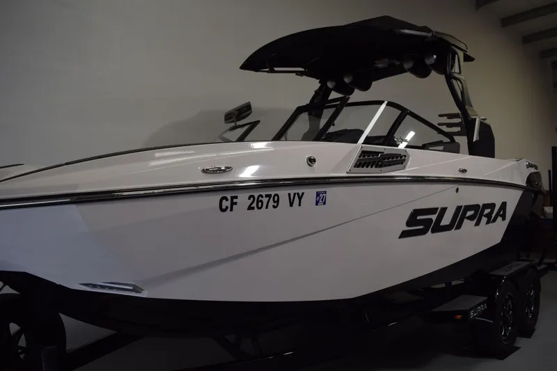 The Image of 2023 Supra SA boat in showroom, sleek design, white exterior, black accents. - 1