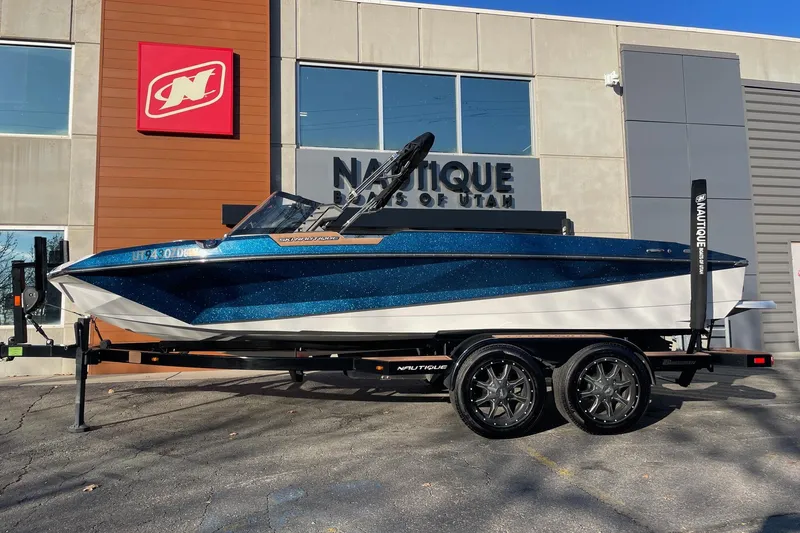 The Image of 2023 Nautique Ski Nautique boat on trailer outside dealership, blue and white design. - 1