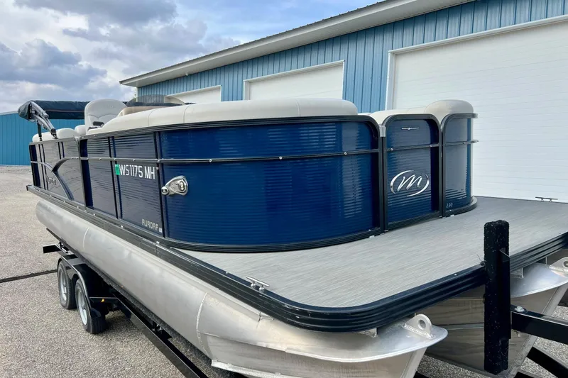 Slide: The Image of 2018 Manitou 23 Aurora LE pontoon boat on trailer, parked near blue building. - 4